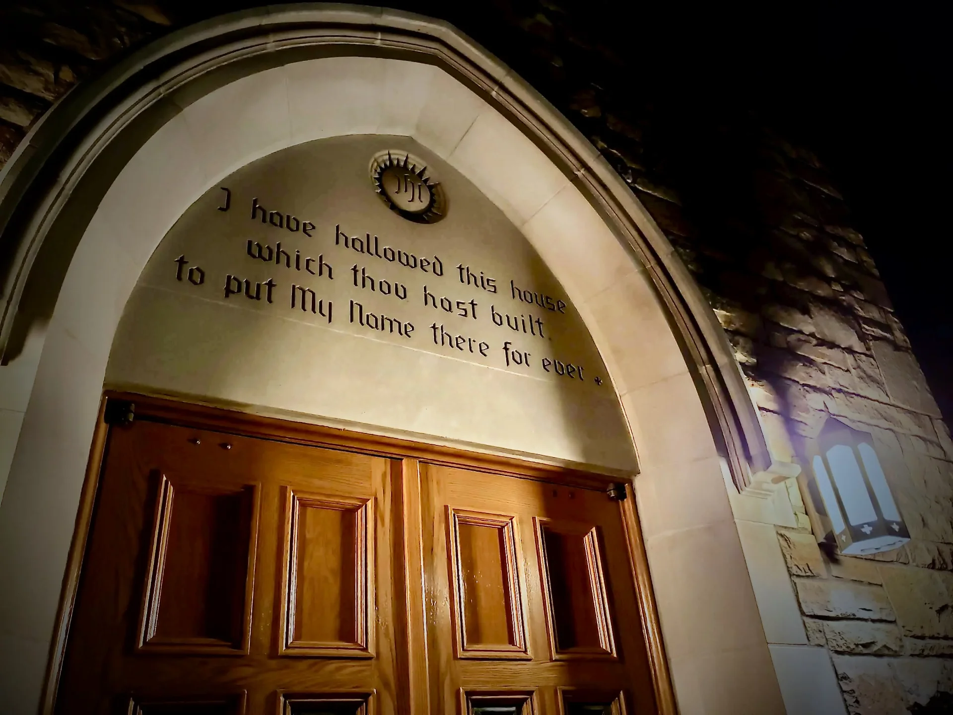 Zion Lutheran Church's arched stone entrance lit at night, carved with the words 'I have hallowed this house which thou hast built, to put My Name there for ever'